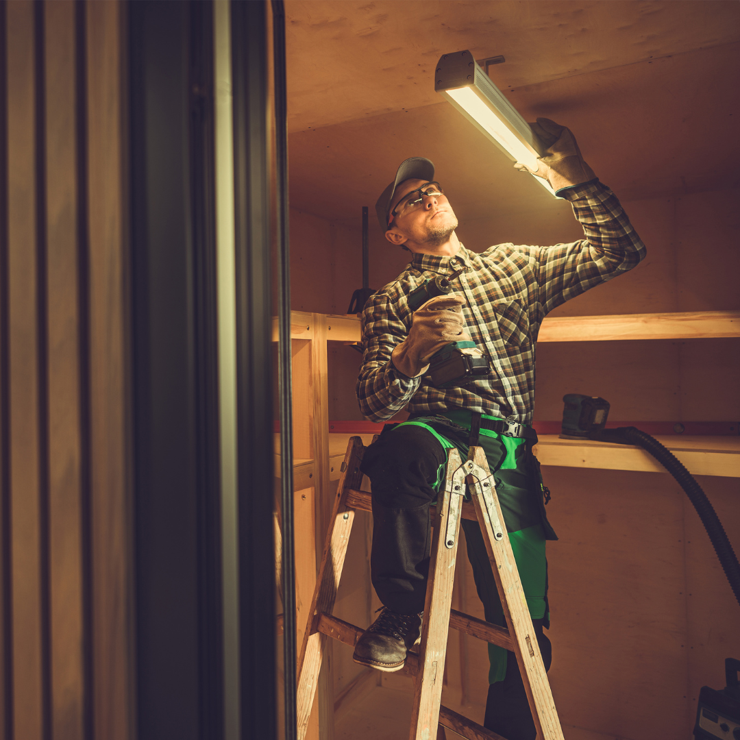 electrical contractor in plaid shirt on a ladder fixing light in room